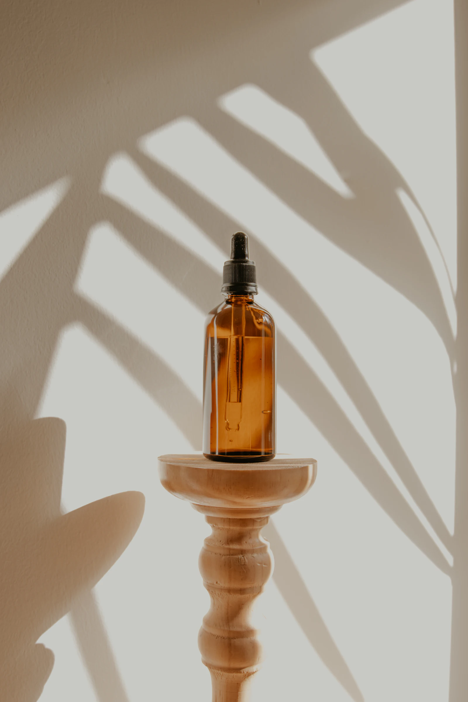 Frasco ámbar de aceite sobre un pedestal de madera con sombras de hojas